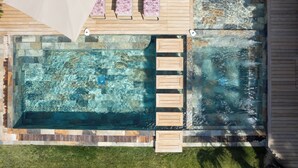 Vista aérea de una piscina con muelle de madera y sillones de descanso.