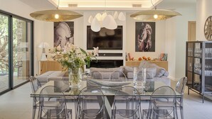 Una sala moderna con una mesa de comedor de vidrio, sillas transparentes, un sofá y dos lámparas colgantes.