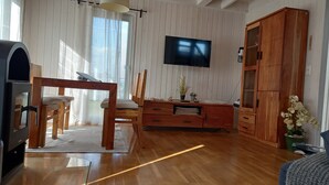 Ett rum med trägolv, en tv som är monterad på väggen, ett träskåp och ett matbord med stolar.