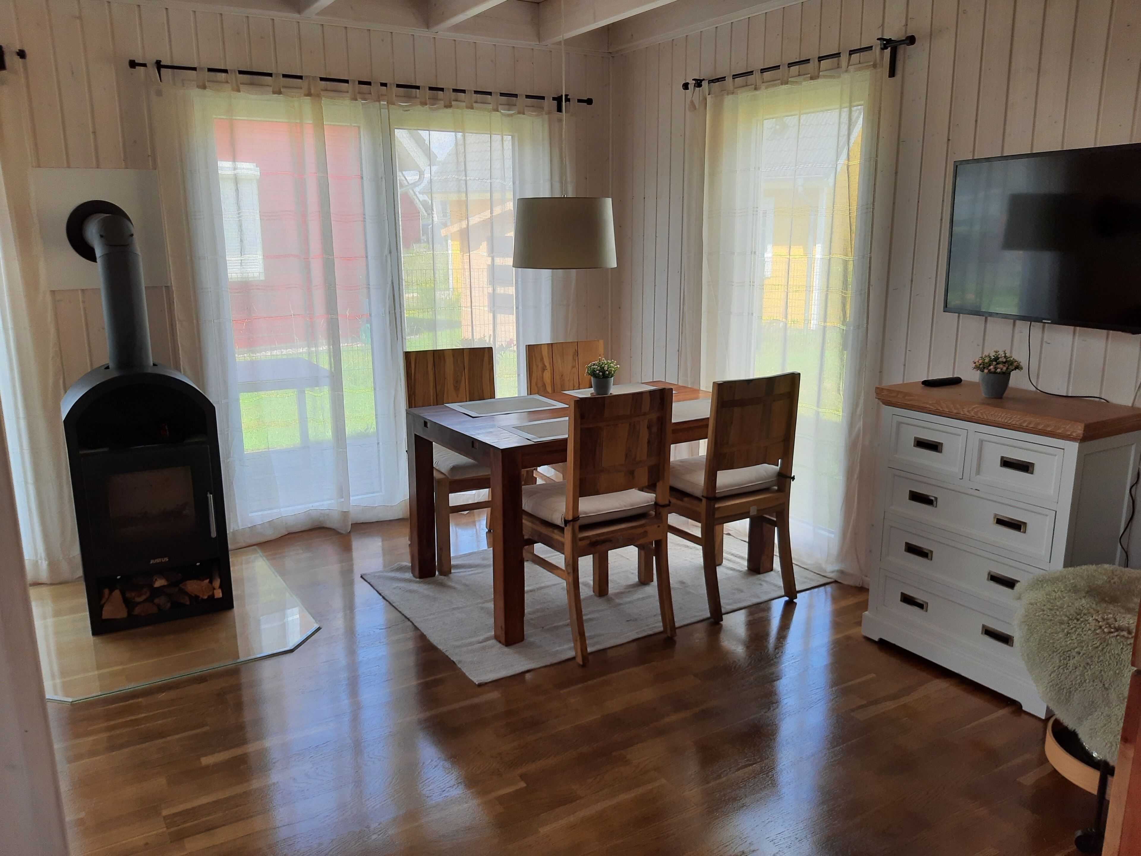 Ein gemütliches Zimmer mit Holztisch, Stühlen, einem Fernseher, einem Kamin und einem Fenster mit Vorhängen.