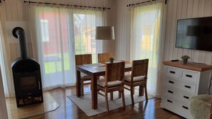 Ett mysigt rum med ett träbord, stolar, en tv, en öppen spis och ett fönster med gardiner.