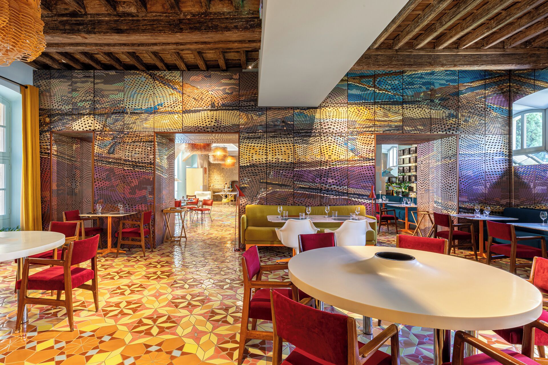 A restaurant with a patterned floor, wooden ceiling beams, and red chairs.