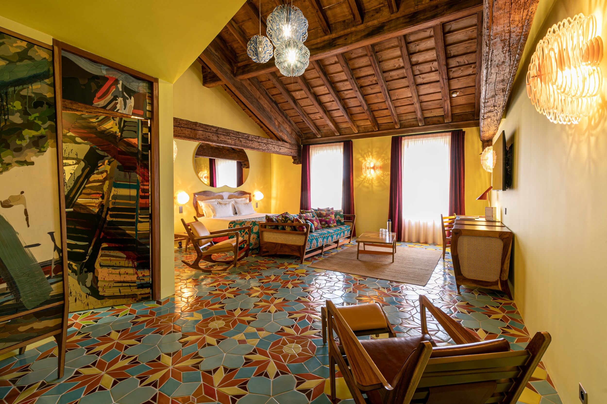 A room with a wooden ceiling, a bed, a sofa, a dining table, and a chair.