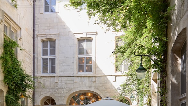 A courtyard with outdoor seating, a fountain, and a building with arched windows. - L'Arlatan (Arles)