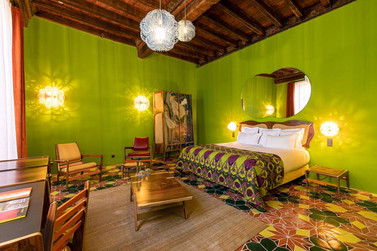 Quarto com uma cama, duas cadeiras, uma mesa e um espelho.