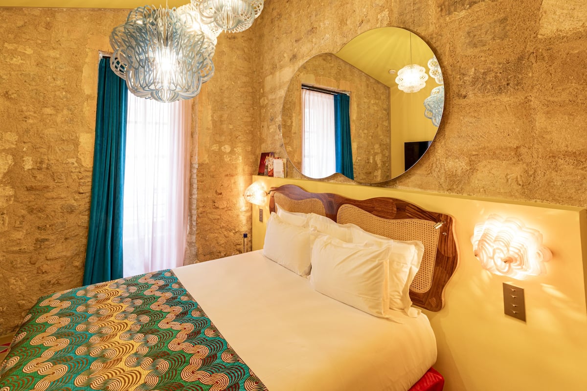 Um quarto com uma cama, um espelho redondo, um candelabro e uma luminária na parede.