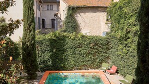 A rectangular pool with a tiled edge, surrounded by greenery and stone buildings. - L'Arlatan (Arles)