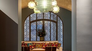 A lobby with a patterned floor, a sofa with colorful cushions, a potted plant, and a decorative ceiling light. - L'Arlatan (Arles)