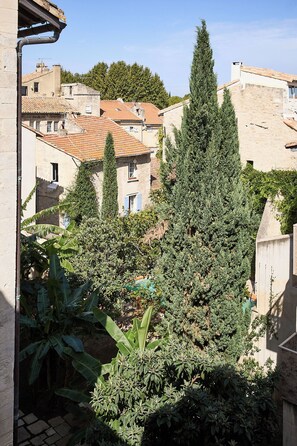 Une cour intérieure agrémentée d’un grand arbre à feuilles persistantes, d’un bananier et de bâtiments en pierre surmontés de toits en tuiles.