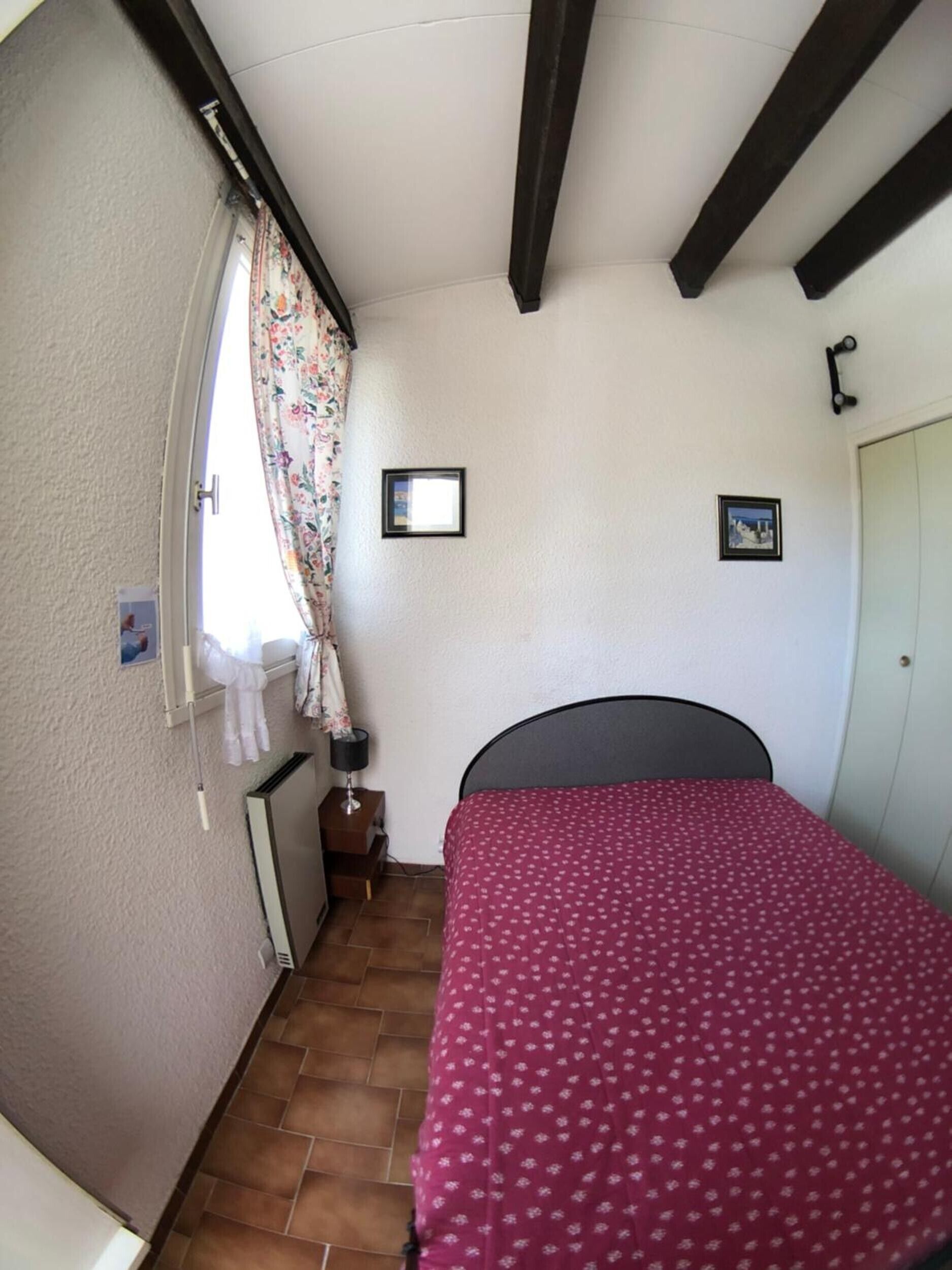 Een slaapkamer met een bed, een raam met gordijnen, een radiator en een deur.