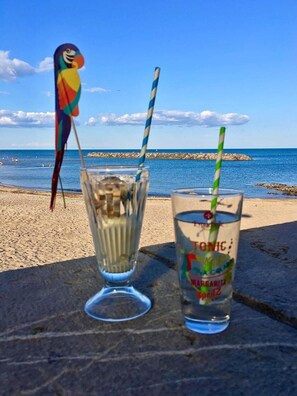 A beach scene with a colorful parrot, two drinks with straws, and a clear view of the ocean. - Apartment 'Marina Oportoducap' with Lake View, Private Terrace and Air Conditioning (Agde)