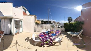 A patio with a table and chairs, a covered seating area, and a view of the sea and buildings. - Apartment 'Marina Oportoducap' with Lake View, Private Terrace and Air Conditioning (Agde)