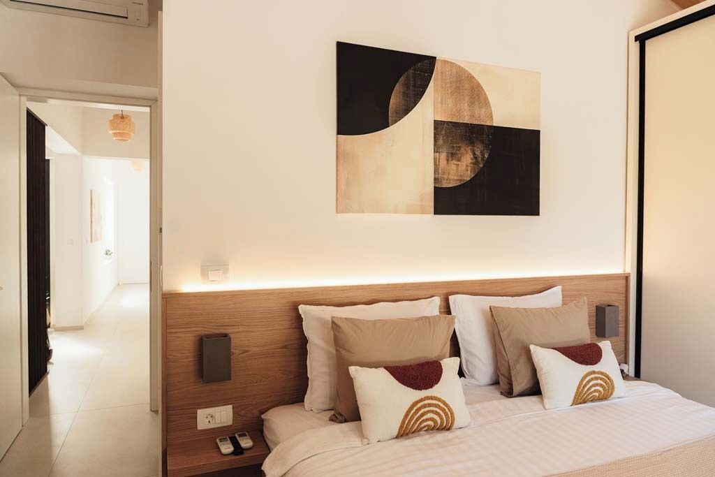 Quarto de hotel com cabeceira de madeira, cama com várias almofadas, obra de arte na parede e mesa de cabeceira com telefone.