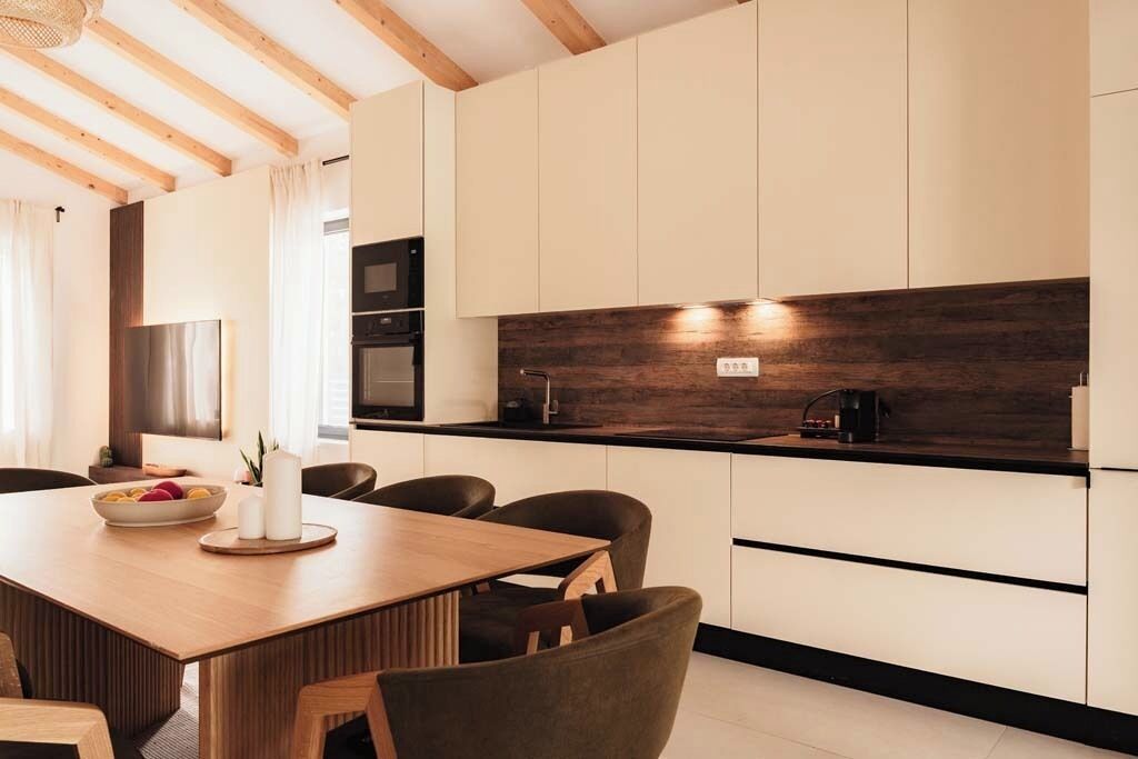 Une cuisine moderne avec des poutres en bois, une table à manger avec des chaises et un four encastré.
