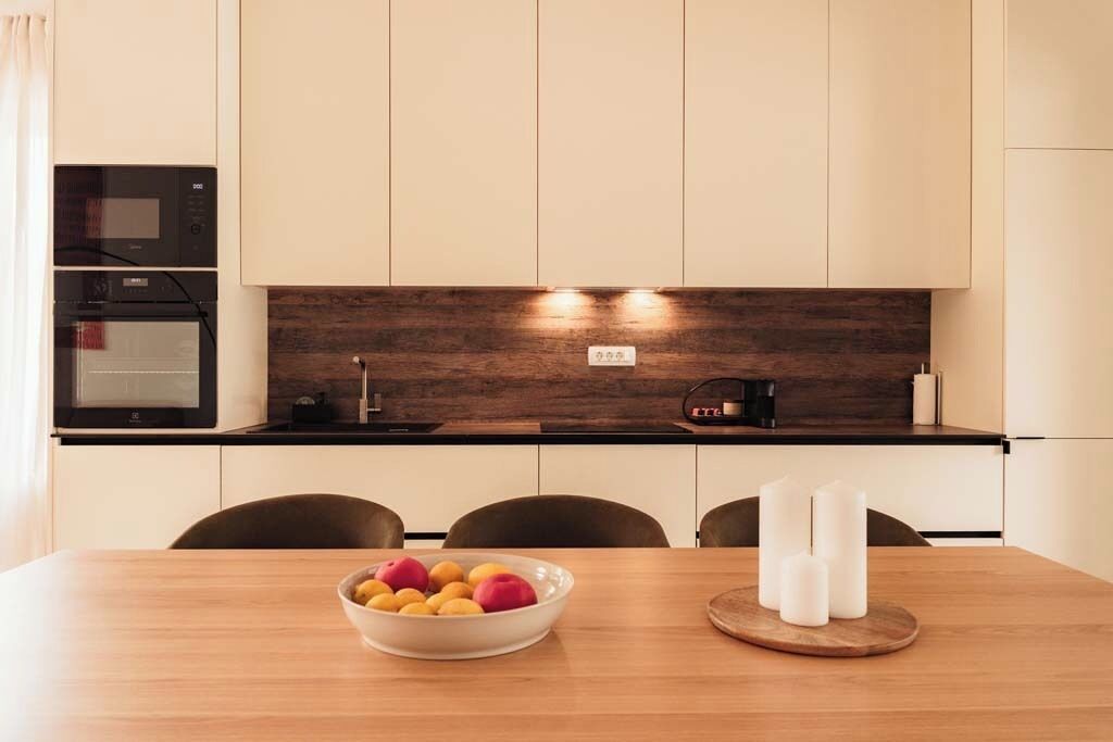 Eine moderne Küche mit einer Holzauskleidung, integrierten Geräten und einem Esstisch mit Obstschale und Kerzen.