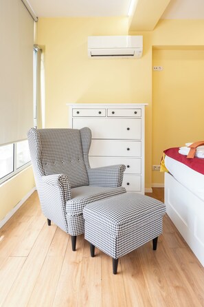 Ein Zimmer mit einem hundszahn-gemusterten Sessel und Hocker, einer weißen Kommode und einer Klimaanlage an der Wand.