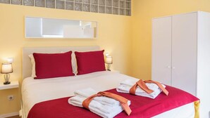 Quarto de hotel com uma cama, dois travesseiros vermelhos, cabeceira branca e dois abajures de cabeceira.