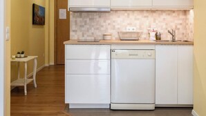 Uma cozinha compacta com armários brancos, lava-louças e painel de azulejos.