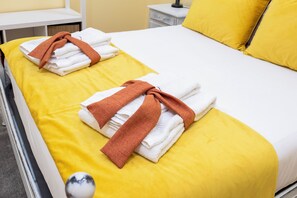 Ein Hotelzimmer mit einem Bett, gelber Bettwäsche, weißen Handtüchern und einem braunen Handtuch.