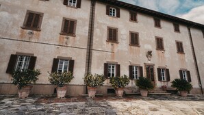 A building with multiple windows and doors, potted plants in front, and a cobblestone ground. - Luna - Villa Cenami - big POOL with view (Massarosa)