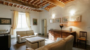 A living room with a sofa, a coffee table, a wooden cabinet, and a chair. There are curtains on the windows, and artwork on the walls. - Luna - Villa Cenami - big POOL with view (Massarosa)