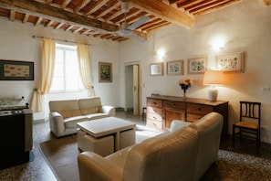 A living room with a sofa, a coffee table, a wooden cabinet, and a chair. There are curtains on the windows, and artwork on the walls. - Luna - Villa Cenami - big POOL with view (Massarosa)