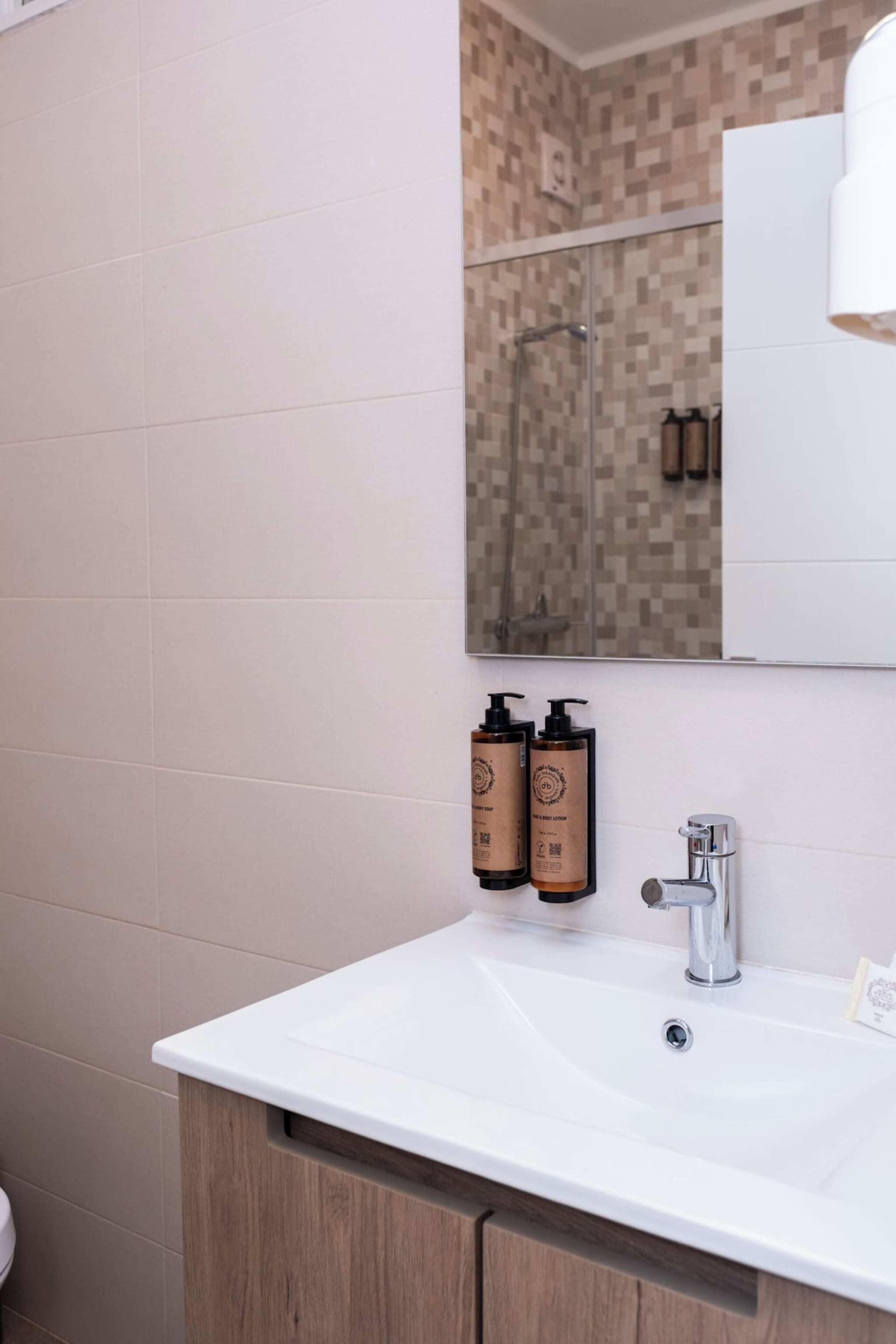 Une salle de bain avec un lavabo blanc, un miroir et deux bouteilles de savon.