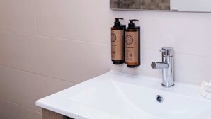 Baño con lavamanos blanco, espejo y dos botellas de jabón.