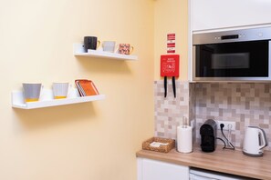Una cocina con armarios blancos, un microondas, una cafetera y un hervidor sobre la encimera.