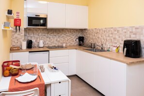 Une cuisine de taille réduite, avec des meubles blancs, un four à micro-ondes, une machine à café et un évier.