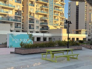 A multi-story residential building with balconies, a sign for 'Downtown By Cityscape,' and outdoor seating areas. - 2-bedroom apartment with AC in Down Town New Alamein (New Alamein)