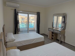 A hotel room with two beds, a vanity with a mirror, and a balcony with a view of buildings.