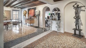 Un ambiente spazioso con soffitto alto, travi in legno a vista, pavimento in pietra lucidato e zona pranzo con sedie e tavolo.