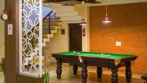 A pool table in a room with a brick wall, a staircase, and a decorative partition. - ELIVAAS Lakeview Manor 3-BHK Luxurious (Bhimtal)