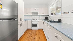 A modern kitchen with white cabinets, a stainless steel refrigerator, a stove, and a blue countertop. - Poppi's Paradise - Jervis Bay Escape | Quiet, Modern & Perfect for Families (Sanctuary Point)