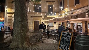 Ein Café mit Außenbereich, Tischen, Stühlen, einem großen Baum und einem Gebäude mit Balkon.
