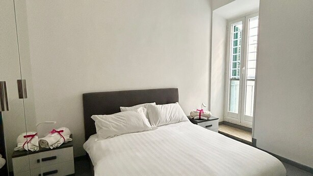 Ein modernes Schlafzimmer mit einem großen Bett, einem Nachttisch mit Lampe und einem Fenster mit Jalousien.