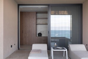 Une chambre moderne dotée d’une porte coulissante donnant sur un balcon, d’une petite table avec un verre de vin et d’un coin salon avec deux fauteuils.