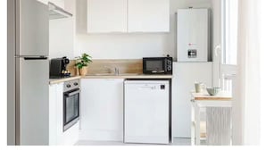 Cozinha compacta equipada com frigorífico, forno, micro-ondas, máquina de lavar loiça e uma pequena bancada.