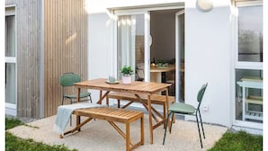 Conjunto de mesa e cadeiras de madeira em área externa, próximo a uma porta de vidro deslizante.