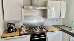 A compact kitchen with white cabinets, a stainless steel range hood, a gas stove, an oven, and a small countertop with a toaster and jars. - APARTMENT 2 P ANTIBES - IDEAL VACATION FOR 2 (Antibes)