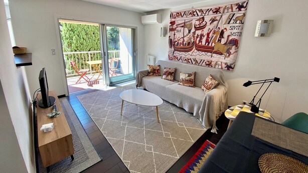 A living room with a sofa, a coffee table, a TV, and a large tapestry. - APARTMENT 2 P ANTIBES - IDEAL VACATION FOR 2 (Antibes)