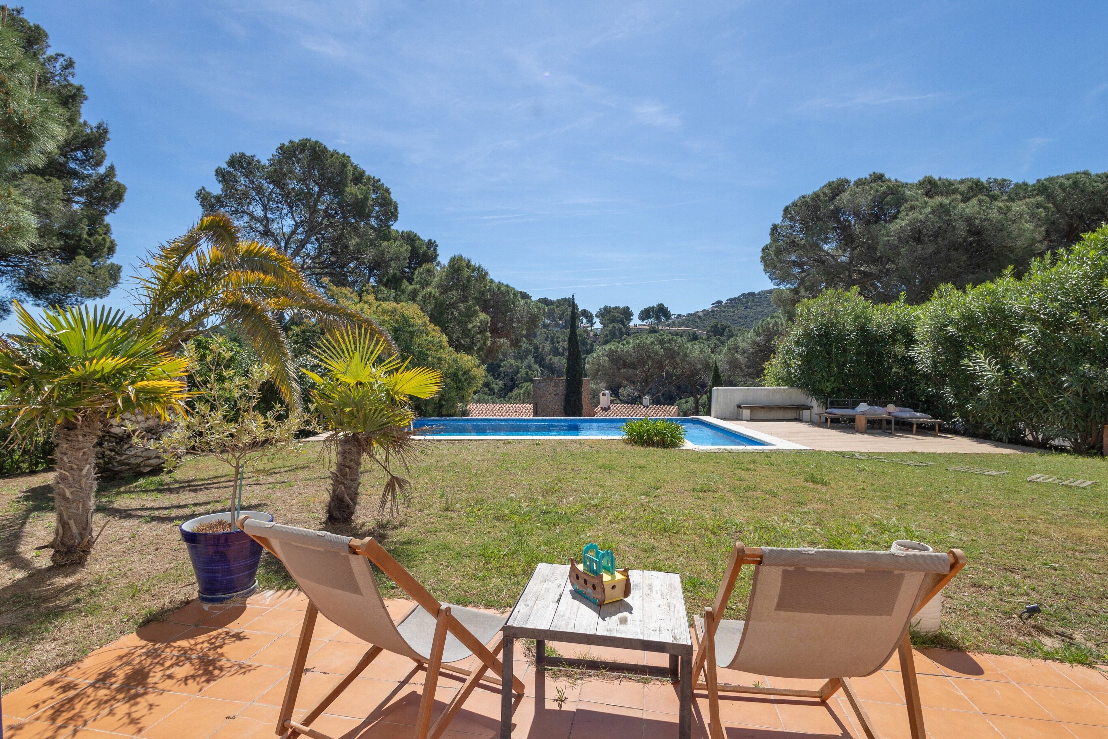 Une terrasse avec deux chaises et une table, une piscine et une vue sur la verdure environnante.