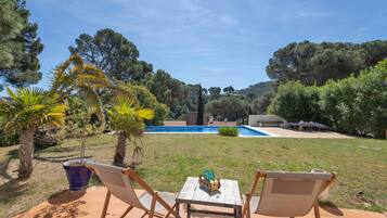 Une terrasse avec deux chaises et une table, une piscine et une vue sur la verdure environnante.