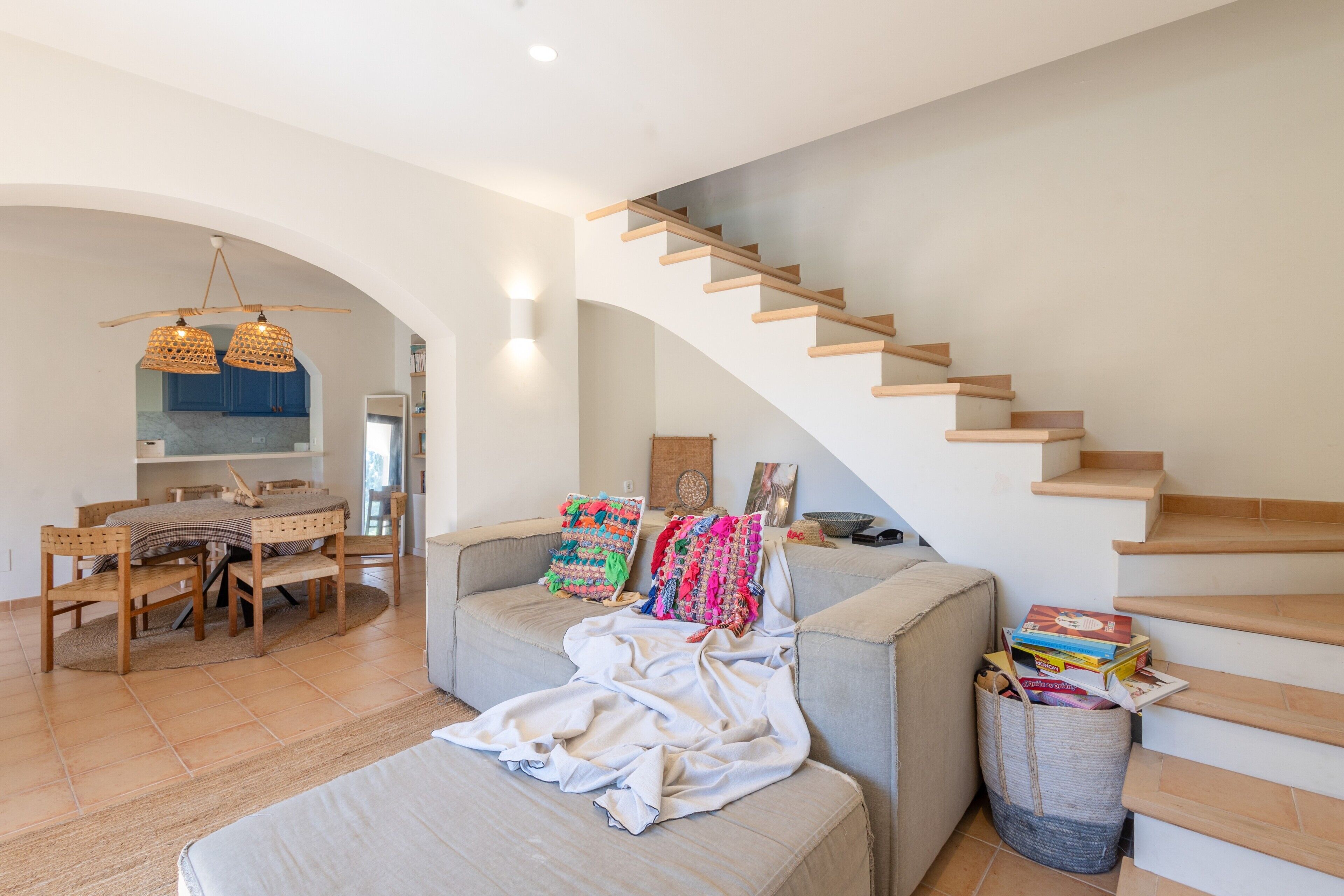 A modern living room with a staircase, a dining area, and a kitchen visible through an archway.