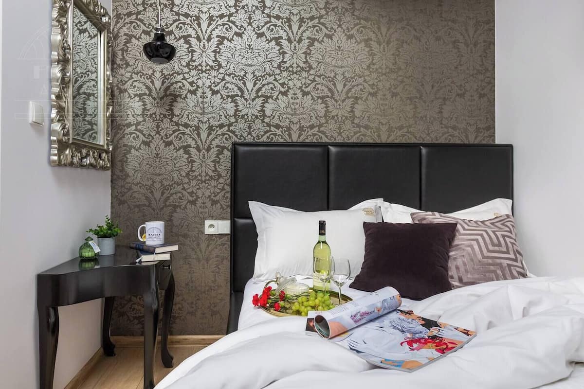 Ein Hotelzimmer mit Bett, Nachttisch mit Lampe, Spiegel und strukturierter Tapete.