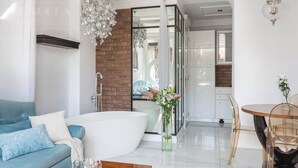 A modern living room with a large white bathtub, a blue sofa, and a dining area with a round table and chairs. - The Eleven by Fragola Apartments (Kraków)