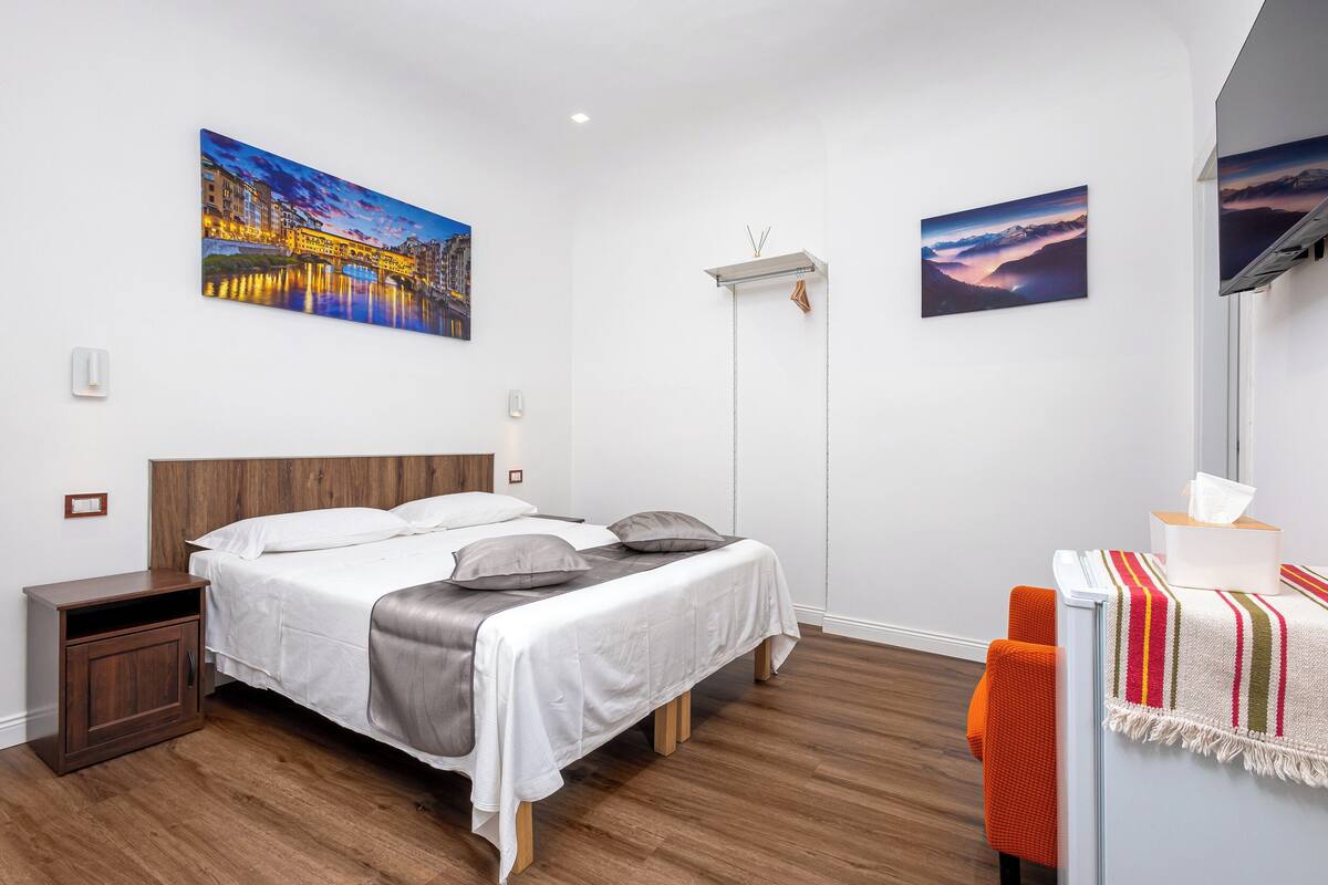A bedroom with a bed, nightstand, bedside table, and a wall-mounted TV.