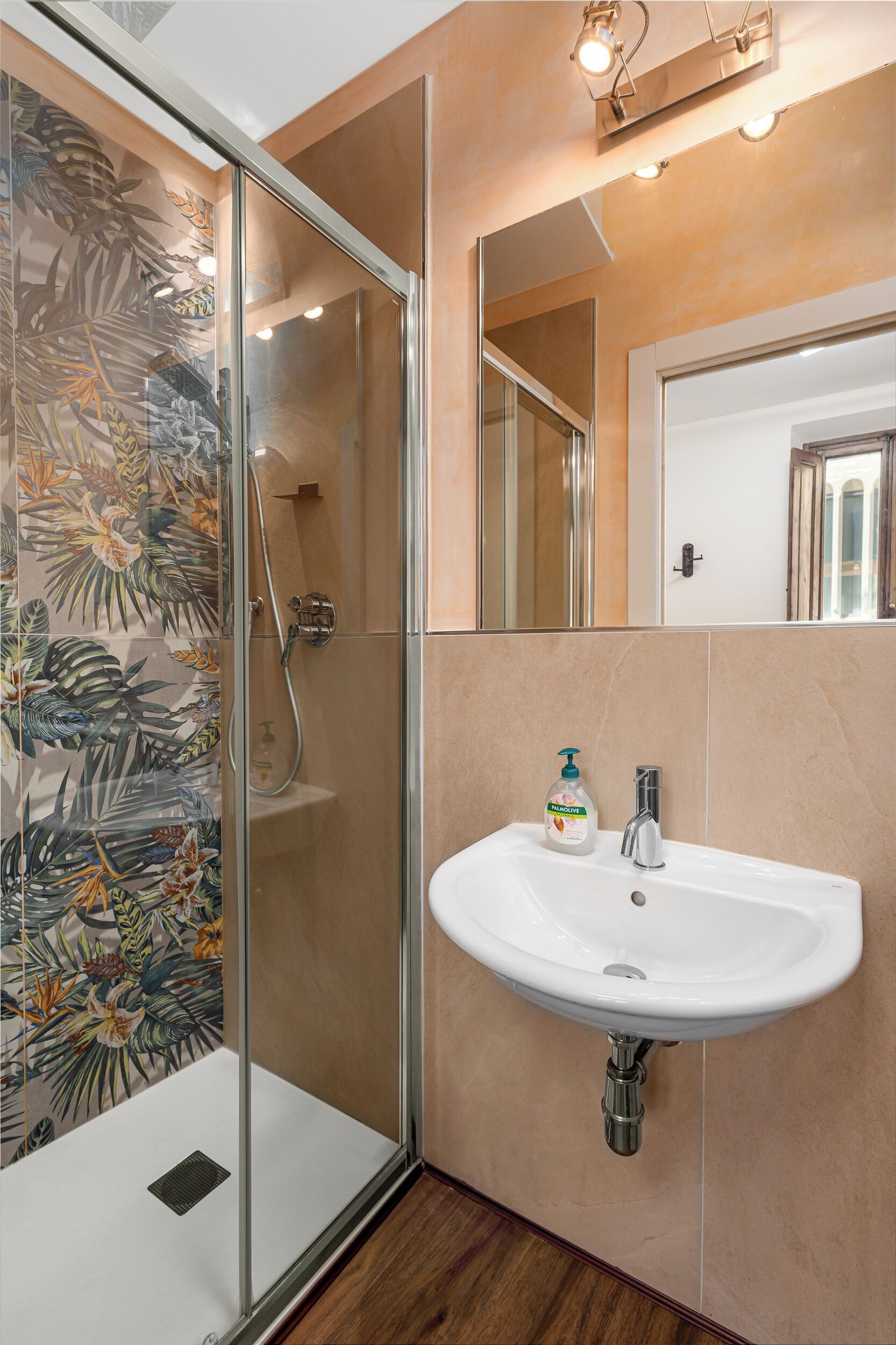 Un baño moderno con cabina de ducha de vidrio, un lavabo blanco con dispensador de jabón y un espejo sobre el lavabo.
