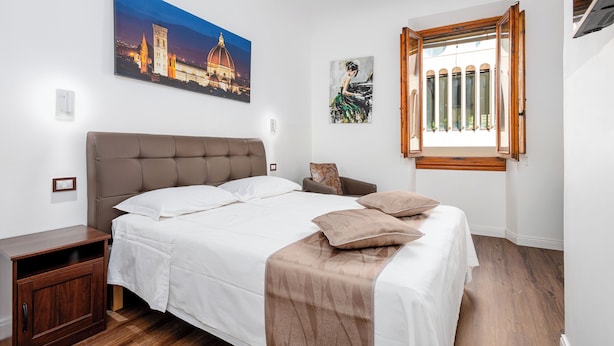 A bedroom with a large bed, a nightstand, a wooden cabinet, a window with a view, and a painting on the wall.